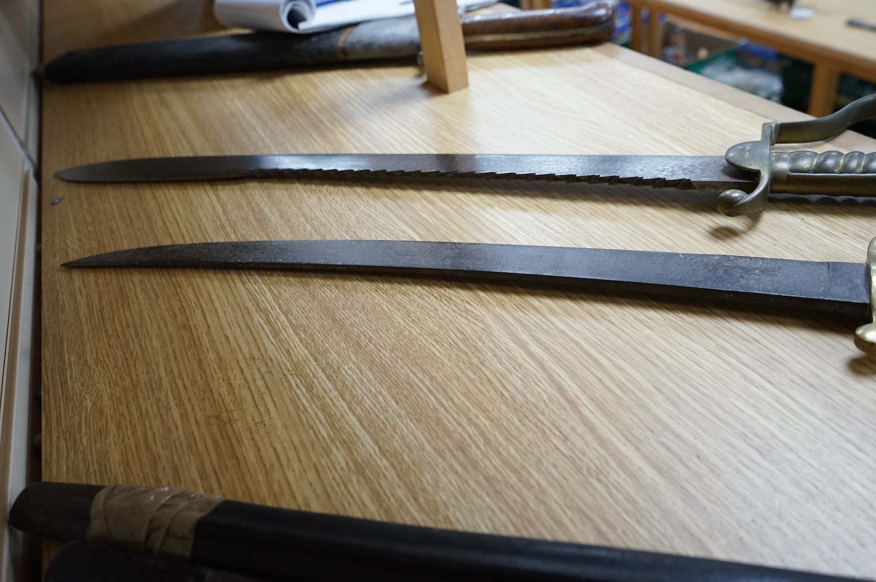 A British Pioneer’s sidearm with brass stirrup hilt, lion’s head pommel and sawback blade, together with an Imperial German sidearm with one piece brass hilt and slightly curved single edge blade